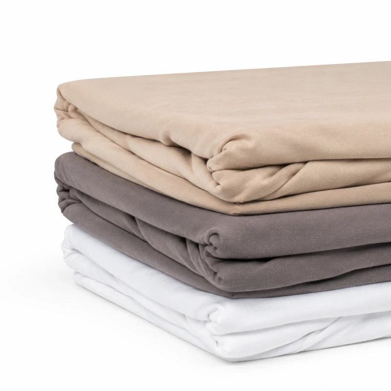 Trois draps housse en coton pliés : beige, taupe et blanc